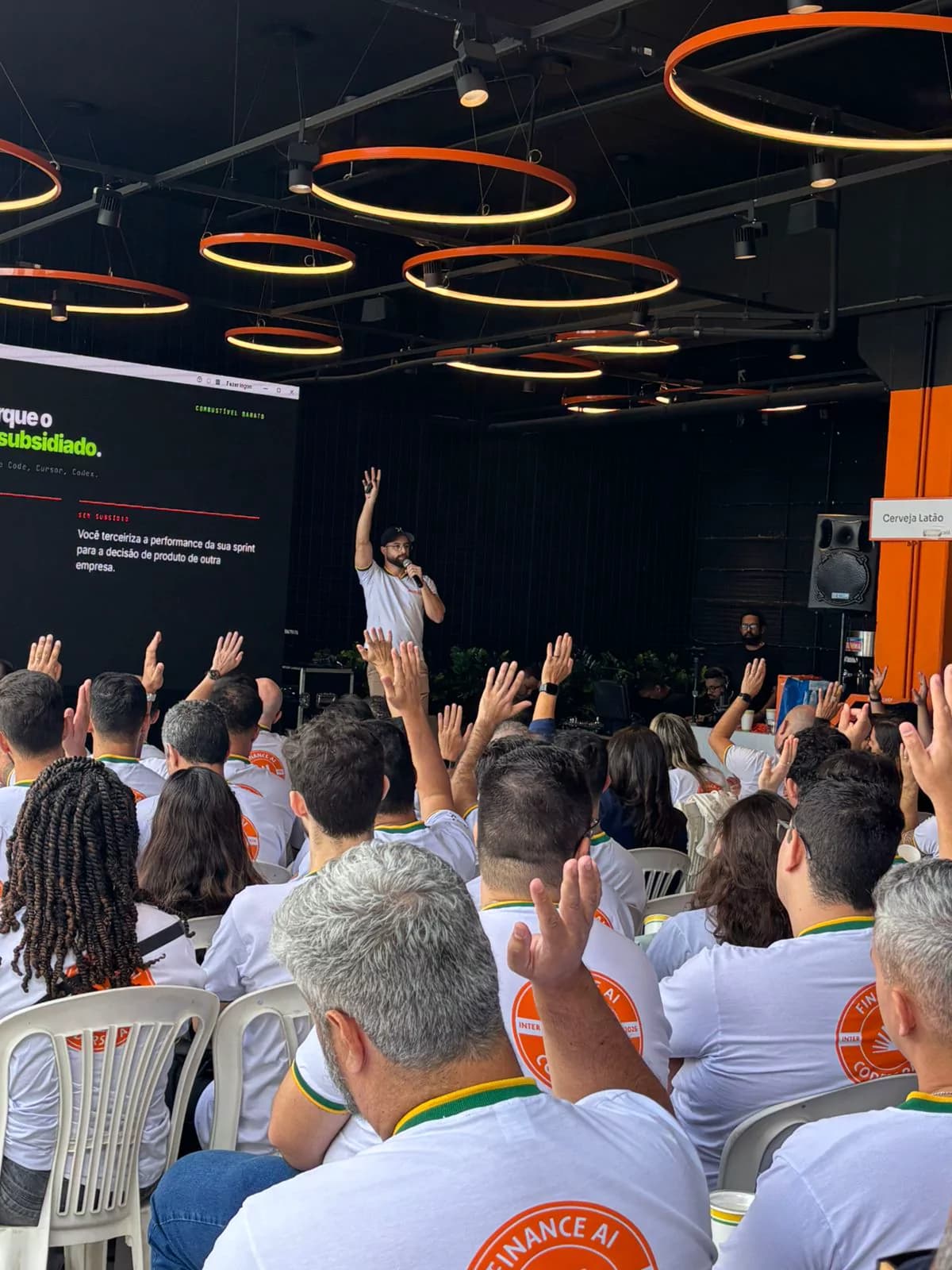 Auditório de um treinamento corporativo com Vinicius Lana, com participantes levantando a mão